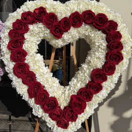 Heart-shaped floral wreath of red roses and white flowers on an easel