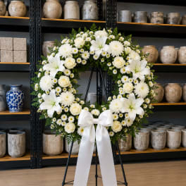 White floral wreath on a black stand with a white ribbon bow