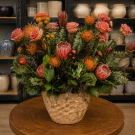 Pink and orange mixed flower arrangement in a textured beige vase