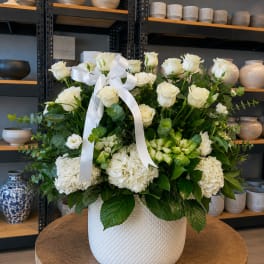 White roses and hydrangeas in a white vase with a ribbon