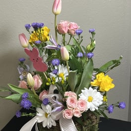 Mixed bouquet with pink tulips, roses, daisies, and purple filler in a moss basket
