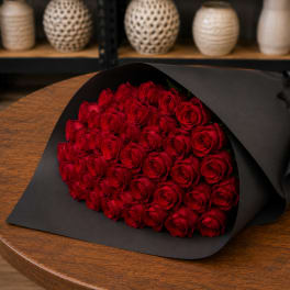 Bouquet of red roses wrapped in black paper on a wooden table
