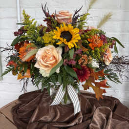 Mixed bouquet with a sunflower, peach roses, and orange blooms in a vase