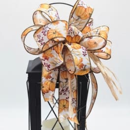 Black lantern with a large pumpkin-pattern ribbon bow and candle inside