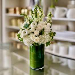 White roses and ranunculus in a tall green glass vase
