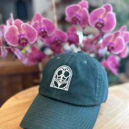 Teal baseball cap on a wooden table with pink orchids in the background