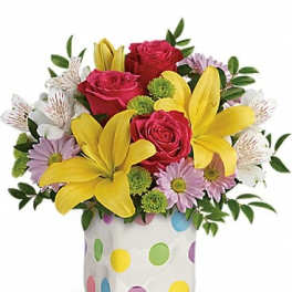 Bouquet of red roses, yellow lilies, and lavender daisies in a polka-dot vase