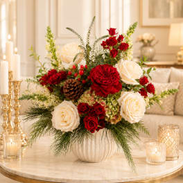 Red and white roses arranged in a white vase with candles nearby
