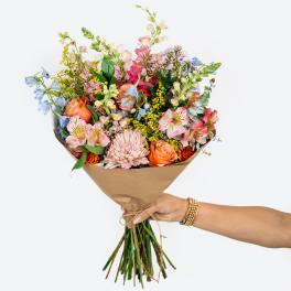 Handheld bouquet of mixed pastel flowers wrapped in brown paper