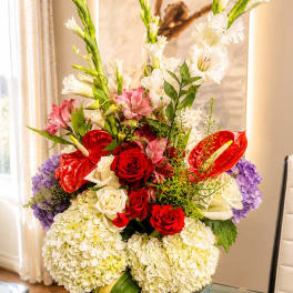 Tall mixed flower arrangement with red roses, white blooms, and purple hydrangeas in a glass vase