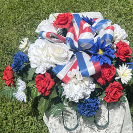 Red, white, and blue floral arrangement with ribbon on a lace-covered stand