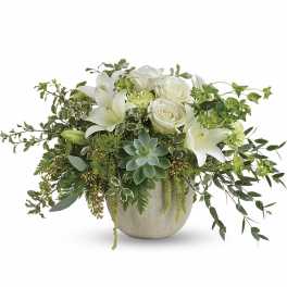 White roses and lilies in a low ceramic vase with trailing greenery