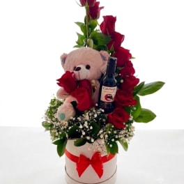 Red roses with a teddy bear and wine bottle in a white hatbox