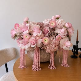 Pink floral arrangement in a textured bowl with cascading bead strands