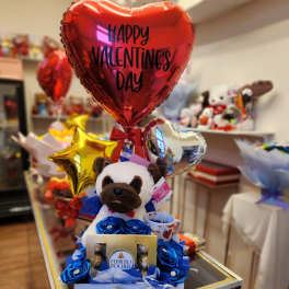 Valentine's gift arrangement with heart balloons, a plush dog, and chocolates