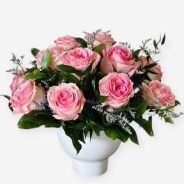Pink roses arranged in a white vase with greenery