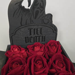 Red roses arranged below a black "Till Death" grave marker