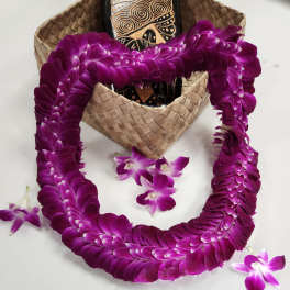 Purple orchid lei draped over a woven hat with a few loose orchid blooms