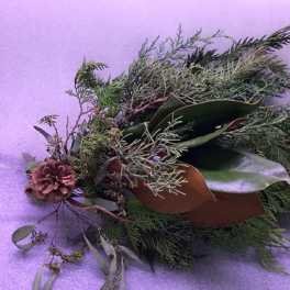 A loose evergreen floral arrangement with a pinecone on a purple background.