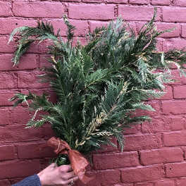 Handheld greenery bouquet tied with a ribbon against a pink brick wall
