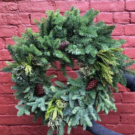 Evergreen wreath with pinecones against a red brick wall