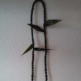 Black braided hanging cord with small green leaves on a wall