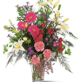 Mixed bouquet with pink gerbera daisies, red roses, white lilies, and carnations in a glass vase
