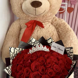 Large teddy bear holding a bouquet of red roses with a tiara
