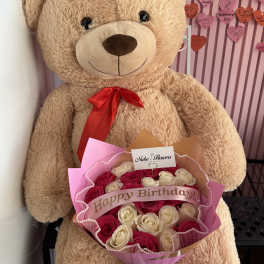 Large teddy bear holding a bouquet of pink and white roses