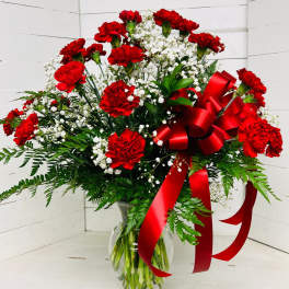 Red carnations and white baby's breath in a clear glass vase with a red ribbon
