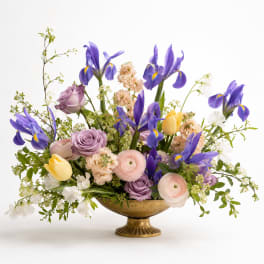 Mixed bouquet of purple irises, roses, and pastel flowers in a gold bowl vase