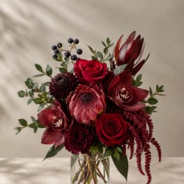 Deep red bouquet in a clear glass vase with roses and tropical blooms