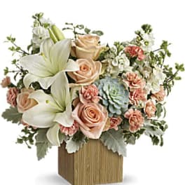 Arrangement of white lilies, peach roses, and carnations in a wooden cube vase
