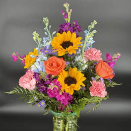 Colorful mixed bouquet in a clear glass vase with sunflowers, roses, and carnations