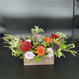 Mixed flower arrangement in a wooden box with orange and lavender roses