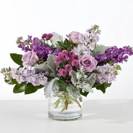 Lavender roses and purple flowers arranged in a clear glass vase