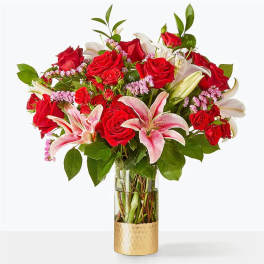 Red roses and pink lilies arranged in a glass vase with a gold base