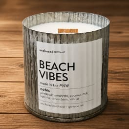 A beach vibes candle in a rustic metal container on a wooden surface