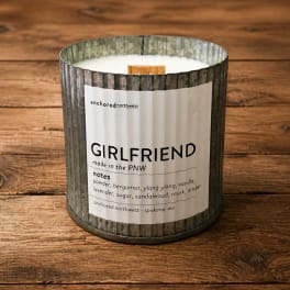 A scented candle in a rustic metal container on a wooden surface