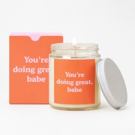 Lit candle in a glass jar with an orange label and matching box