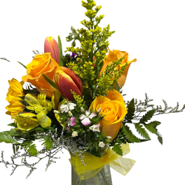 Yellow roses and tulips in a clear glass vase with a yellow ribbon
