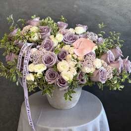Lavender and cream roses arranged in a gray vase with greenery.