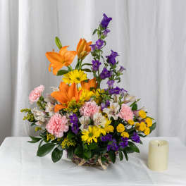 Mixed bouquet with orange lilies, purple bells, pink carnations, and yellow daisies in a basket
