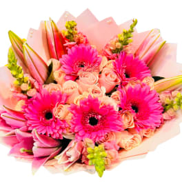 Pink bouquet with gerbera daisies, roses, and lilies wrapped in pale paper