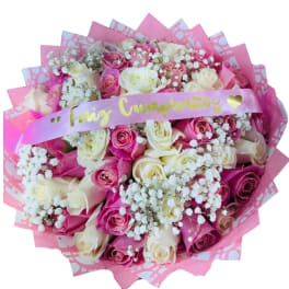 Large round bouquet of pink and cream roses with white baby's breath and a Feliz Cumpleaños ribbon.