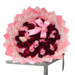 Large bouquet of red and pink roses wrapped in layered pink paper with lace trim and a pink bow.