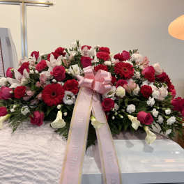 Large pink and red funeral spray with ribbon on a casket