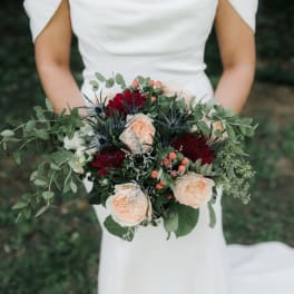 Bride holding a bouquet of peach and burgundy flowers with greenery