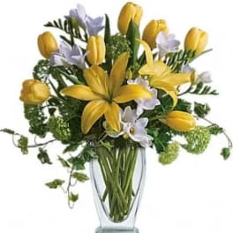 Yellow tulips and pale lavender flowers in a clear glass vase
