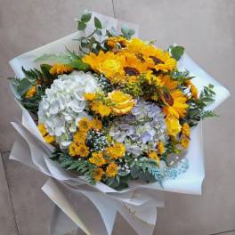 Bouquet of sunflowers, hydrangeas, and yellow roses wrapped in white paper